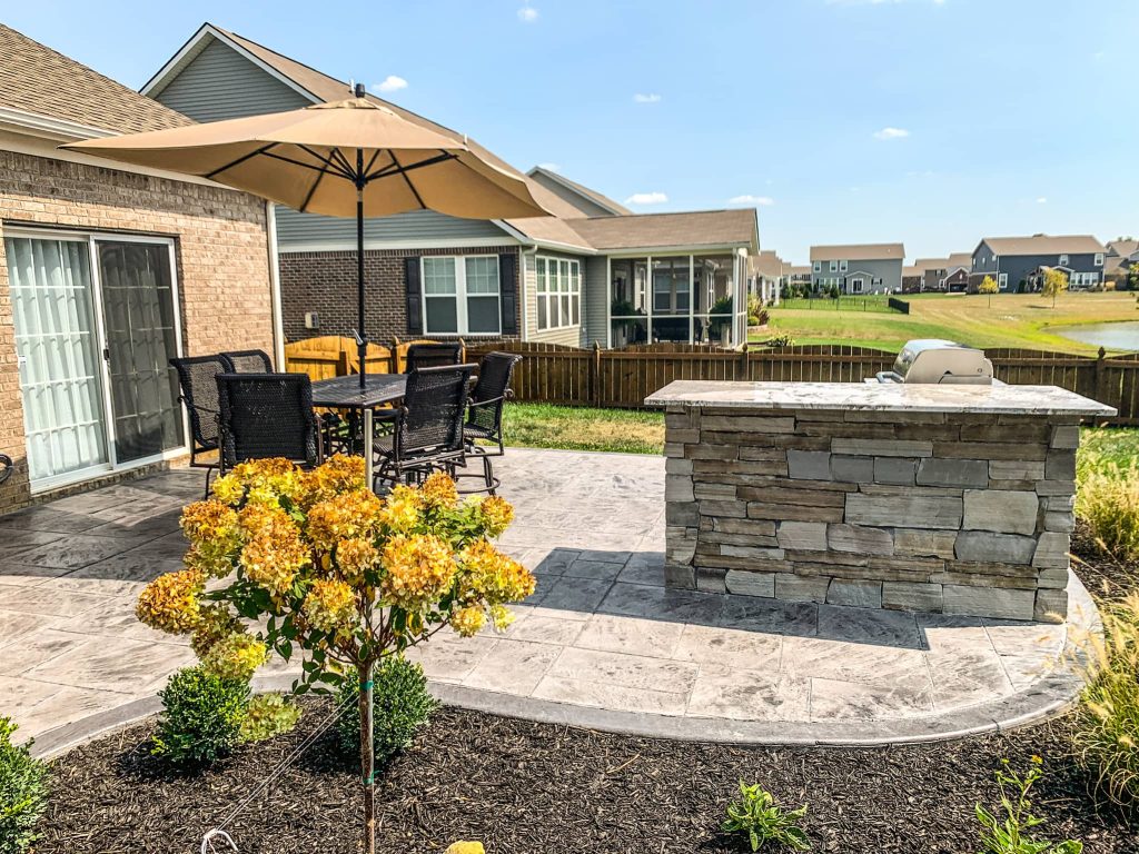 Concrete patio with an outdoor kitchen, grill station, and dining area, set in a modern backyard.