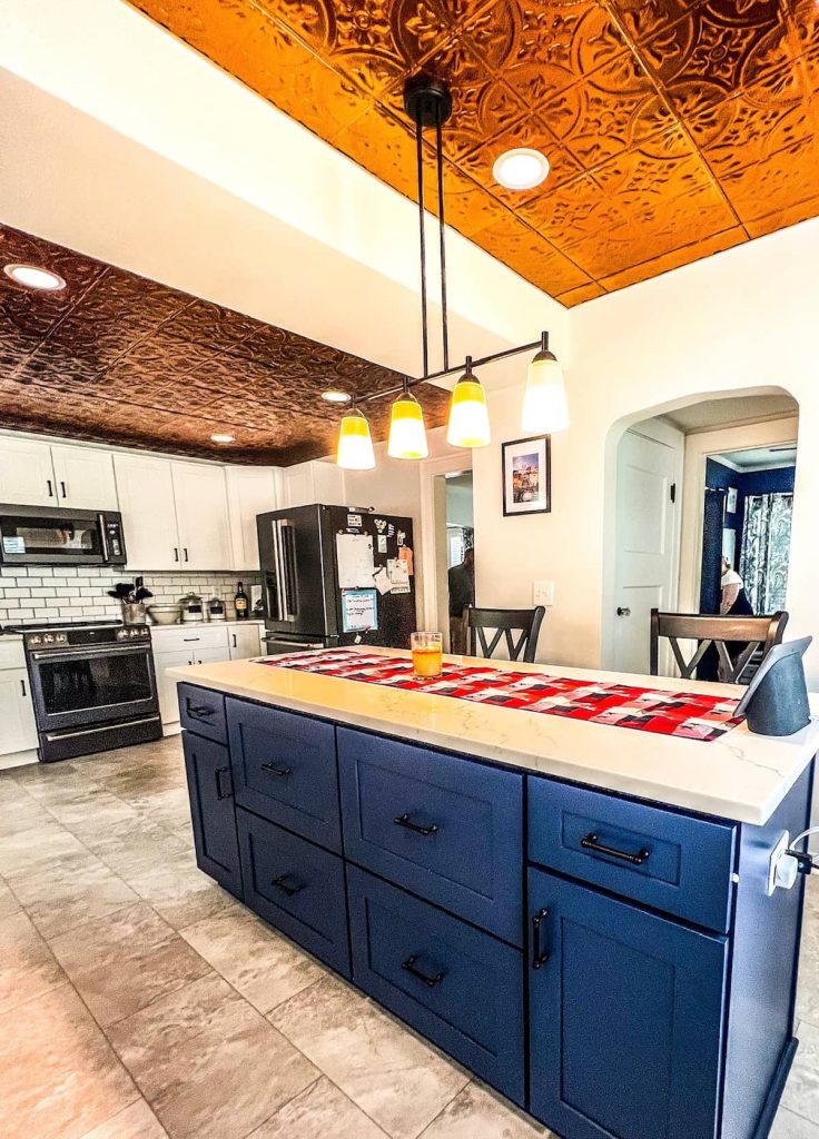 Modern kitchen with a navy blue island, white countertops, and copper ceiling accents