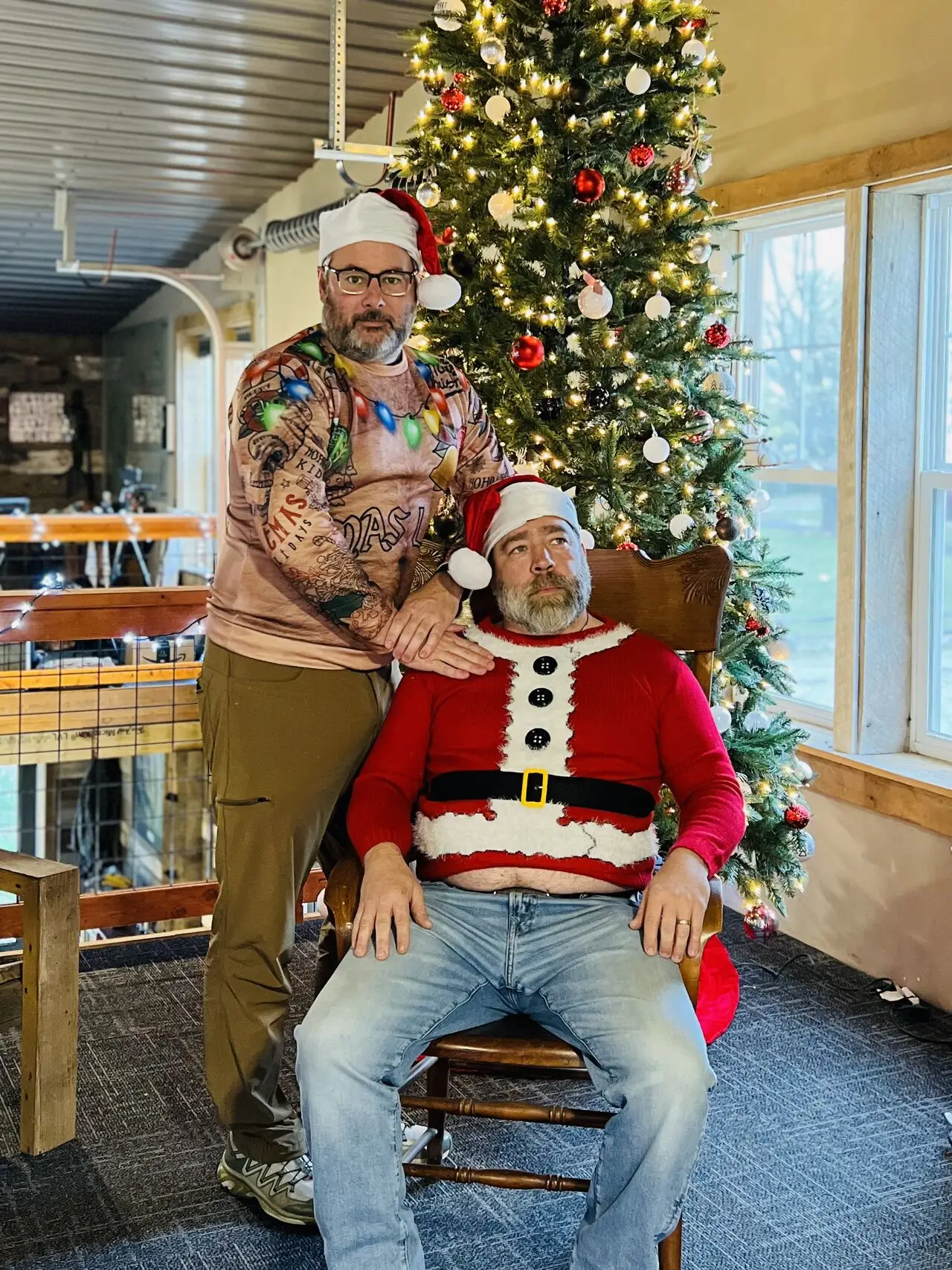 Two members of the BGW Construction team dressed as Santa and his helper posing humorously in front of a Christmas tree, showcasing holiday spirit.