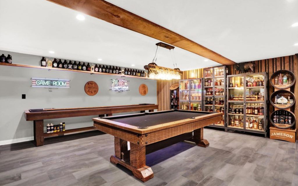 Finished basement speakeasy with custom bar, barrel-style table, shuffleboard, and neon signs