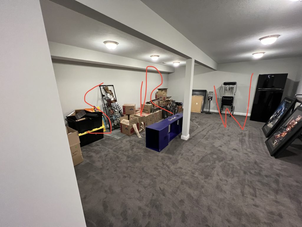 Cluttered basement with exposed carpet and storage boxes before remodeling