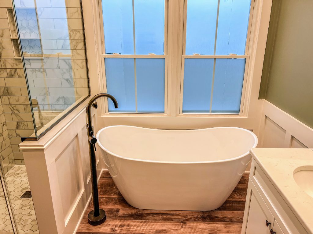 Close-up of a white freestanding soaking tub with bronze floor-mounted faucet in an Avon, Indiana bathroom remodel