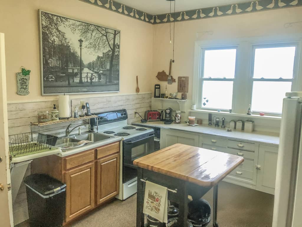 Photo of an older kitchen with mismatched cabinets, vintage appliances, a small island, and wall art.