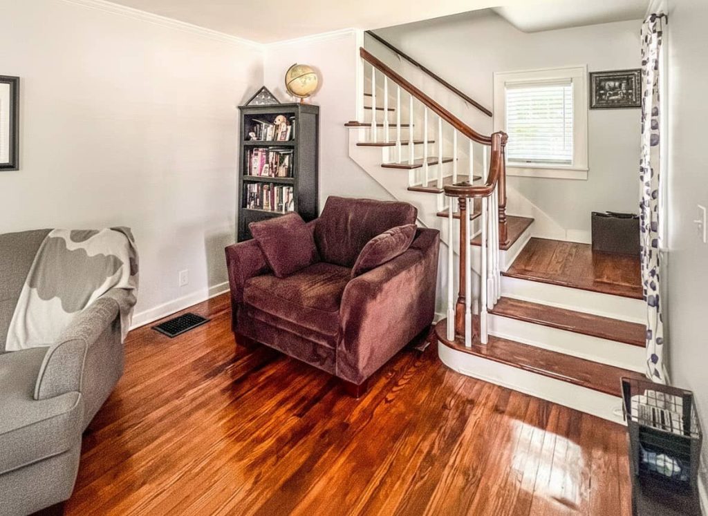 Cozy reading nook in a historic home featuring a plush burgundy armchair, black bookcase, and wood staircase with white risers and dark railing.