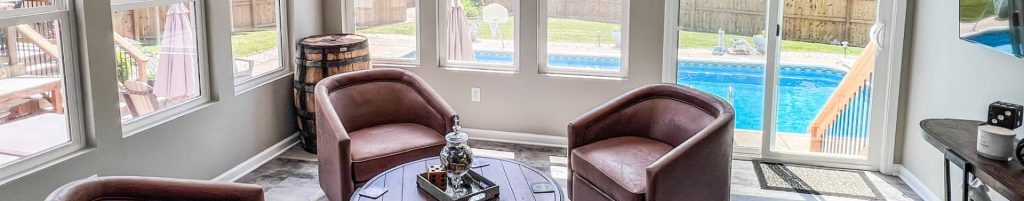 Modern sunroom addition with leather chairs and backyard pool view through large windows.