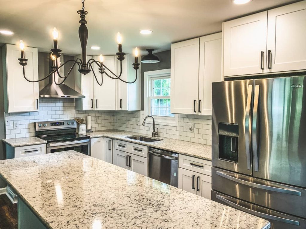 Bright kitchen with white shaker cabinets, subway tile backsplash, granite countertops, stainless steel appliances, and a black chandelier.