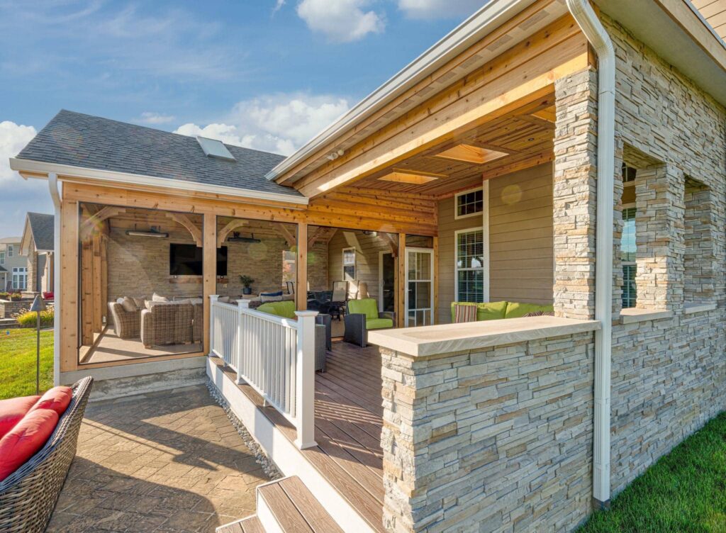 Covered backyard patio with wood ceiling, stone columns, seating area, and screened porch in Brownsburg, Indiana.