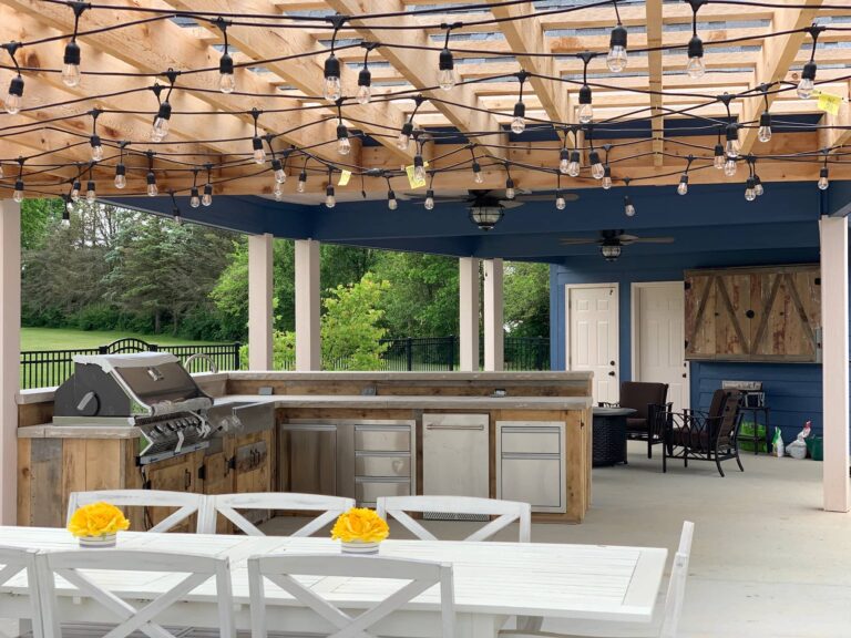 Covered outdoor kitchen with pergola, string lights, stainless steel grill, and bar seating in Plainfield, Indiana.