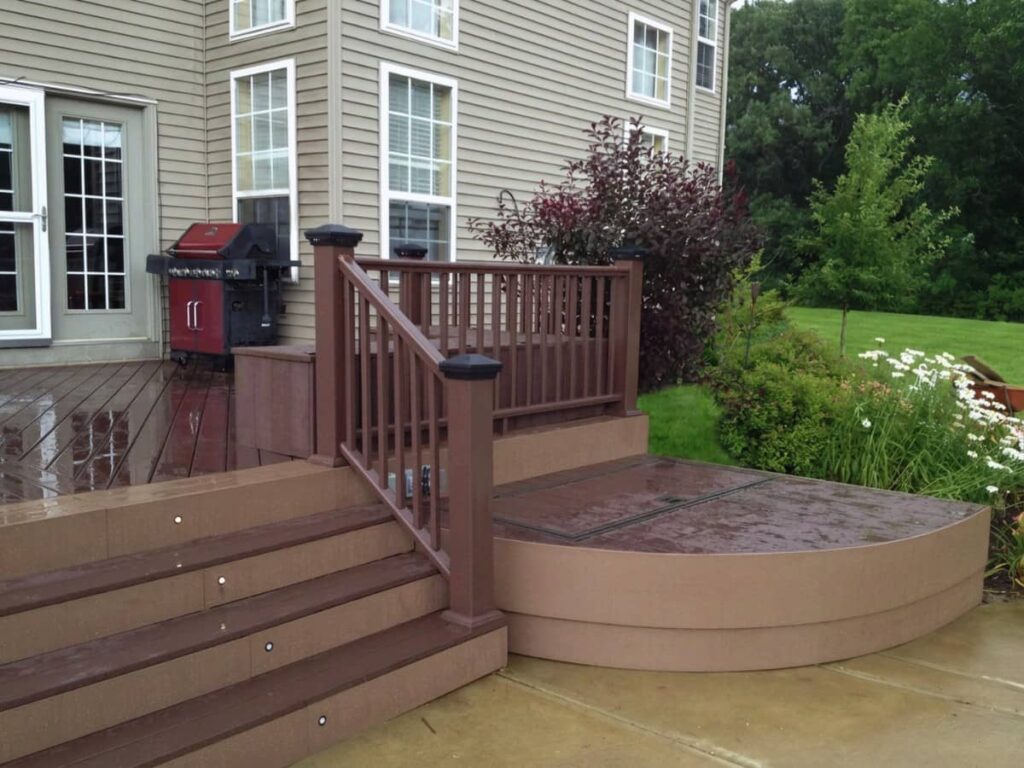Multi-level composite backyard deck with custom railings, wide steps, and a curved platform connected to a home's rear entrance.