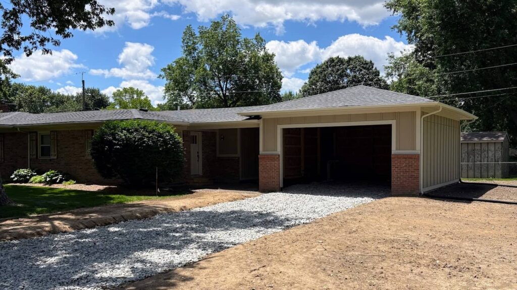 Single-story brick home with a newly constructed attached two-car garage and gravel driveway.