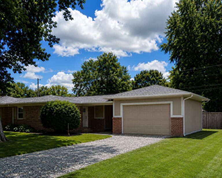 Exterior of a single-story brick home with an attached two-car garage, gravel driveway, green lawn, and mature trees.