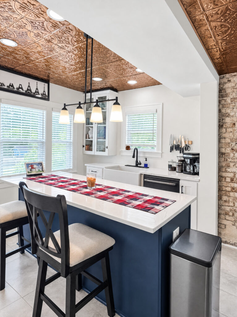 White kitchen with a copper pressed-tin ceiling, exposed original brick and a navy island