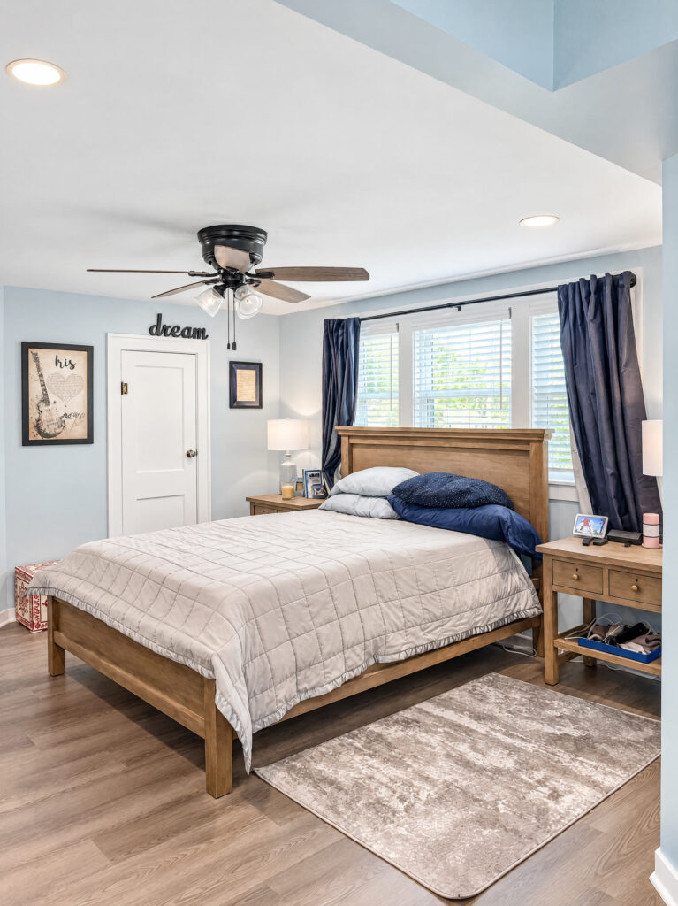 Finished primary bedroom with blue-gray walls, wood bed and updated lighting