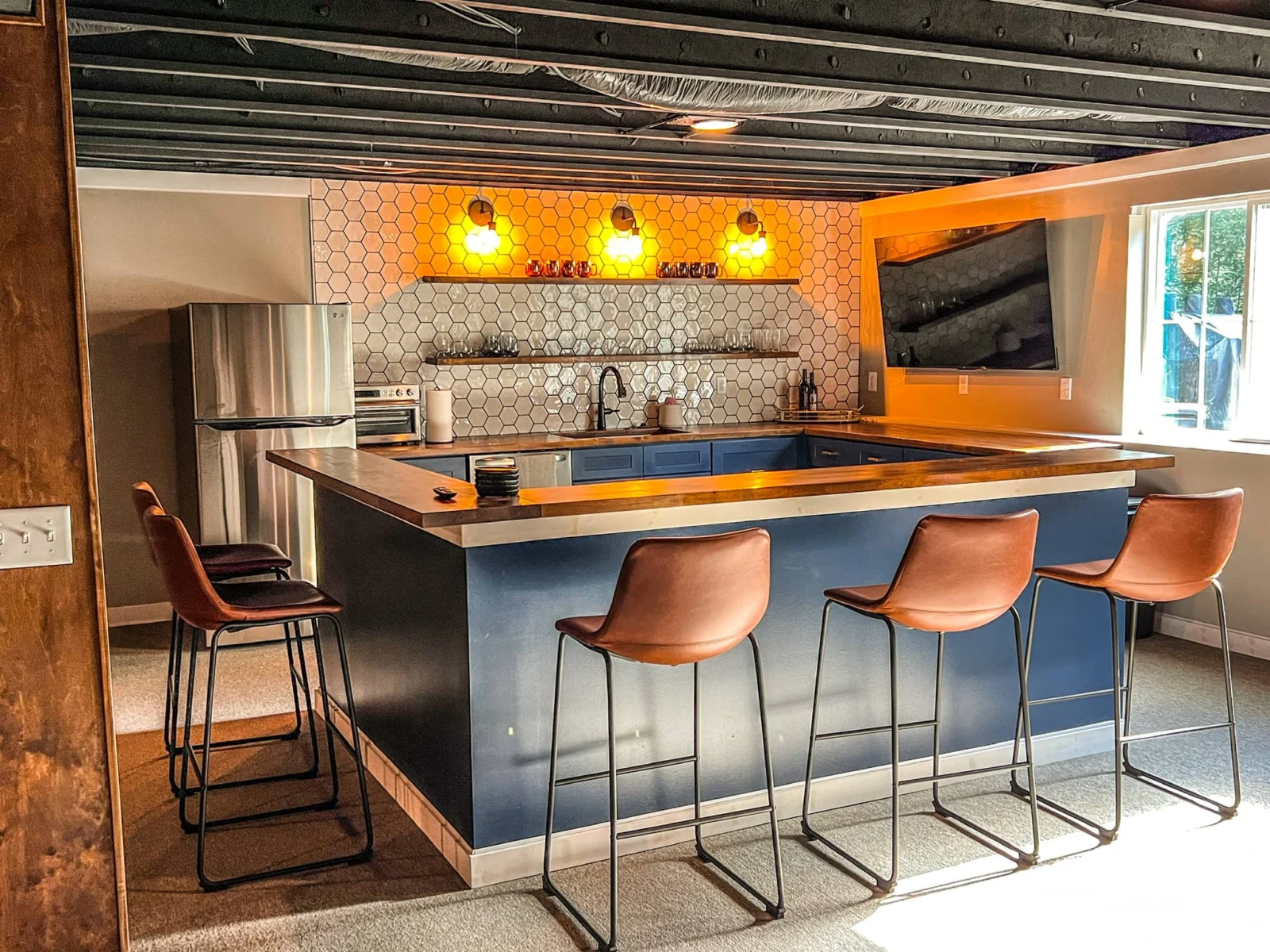 Home bar with blue cabinets, wood counters, hexagonal tile backsplash, and exposed dark ceiling joists.
