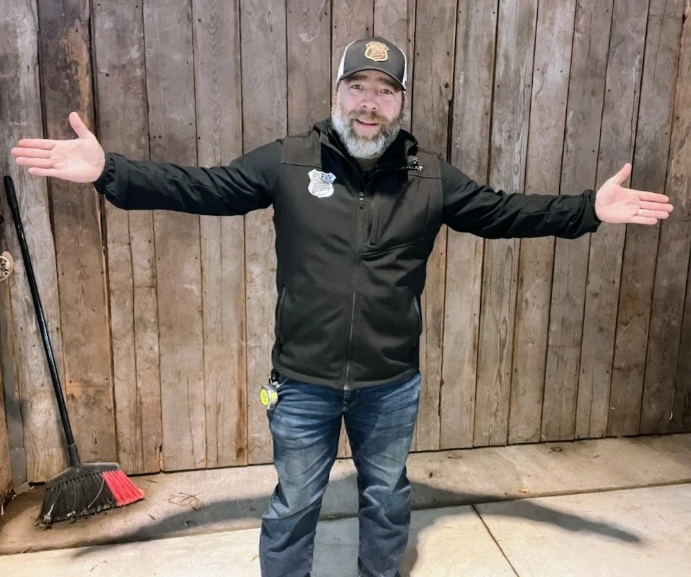 Bobby Williams standing with his arms open in front of wood workshop doors.