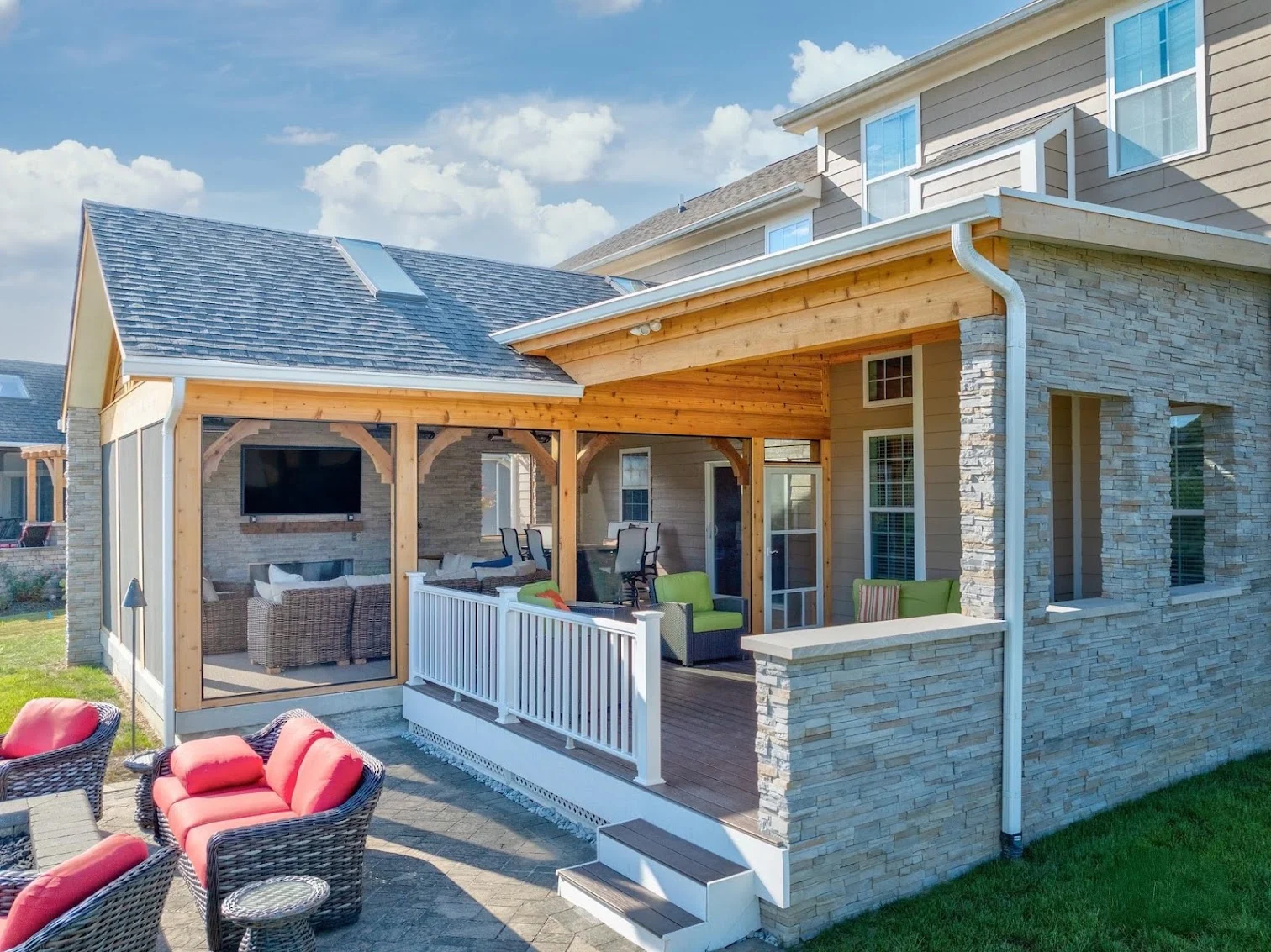 Attached porch with screened seating, a covered deck, stone-clad walls, and steps to a paved patio.