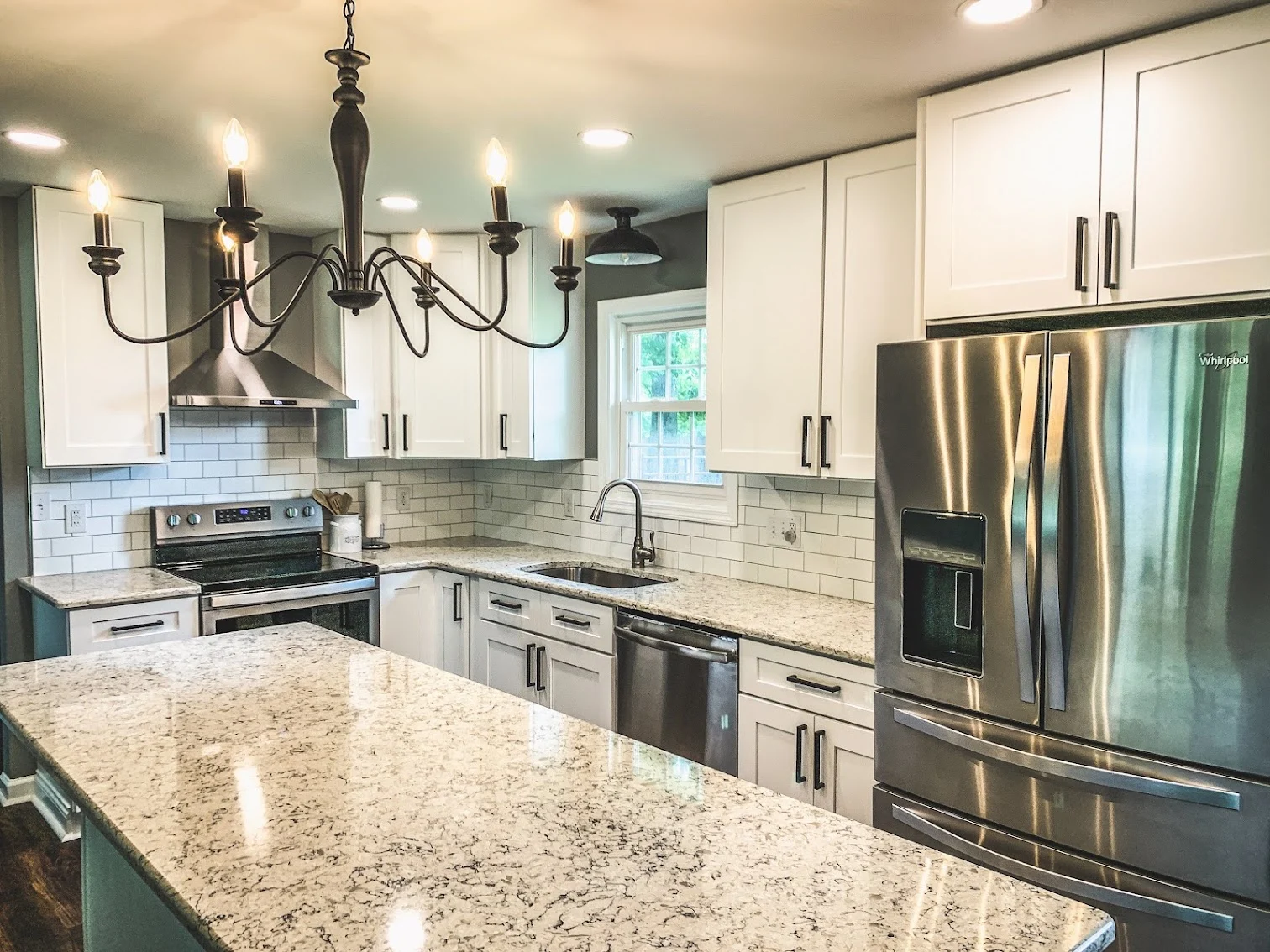 White kitchen cabinets with dark handles, a subway tile backsplash, stainless appliances, and a broad island.
