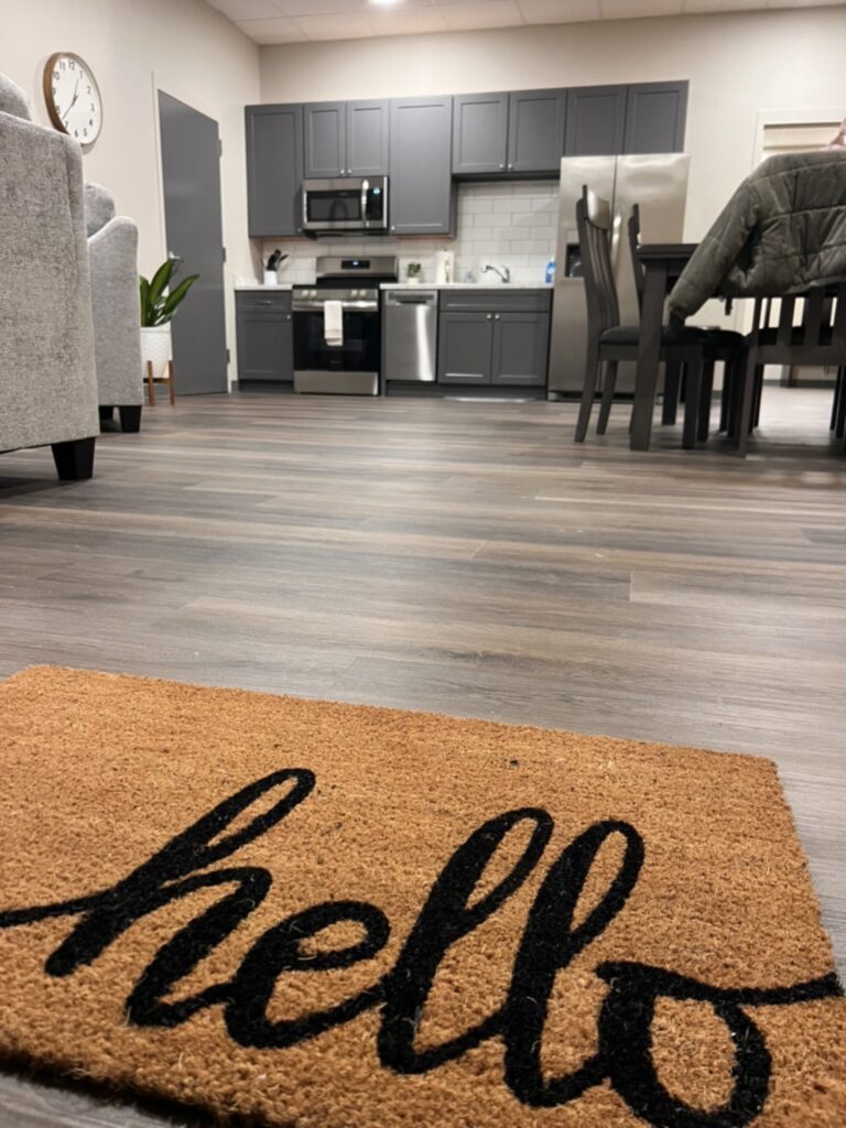 A “hello” doormat at the entrance of the DCS safe space in Avon, Indiana, looking across new residential LVP flooring to the kitchen BGW Construction remodeled