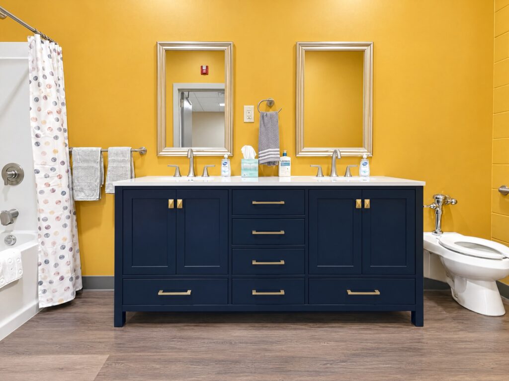 Full bathroom in the DCS safe space in Avon, Indiana, with a navy double vanity, brass hardware, framed mirrors and towel bars installed by BGW Construction