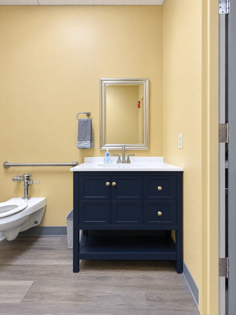 Half bath refresh in the DCS safe space in Avon, Indiana, with a navy furniture-style vanity, framed mirror and towel ring replacing a wall-hung commercial sink