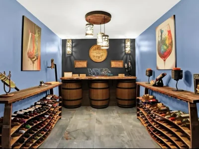 Speakeasy-Basement-7 Secret speakeasy bourbon room with vibrant blue walls, black backsplash, wavy wooden bottle racks, and geometric cutout lighting