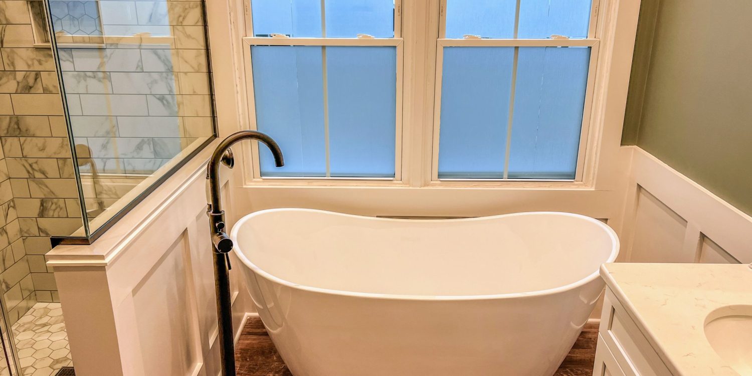 Close-up of a white freestanding soaking tub with bronze floor-mounted faucet in an Avon, Indiana bathroom remodel