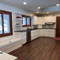 Wide view of a modern kitchen featuring white cabinets, black countertops, and rich wood flooring
