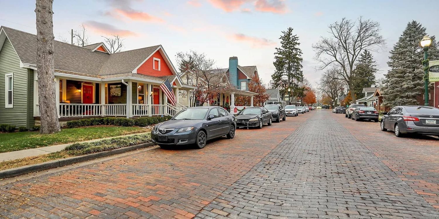 Charming historic neighborhood with colorful renovated homes and cars parked along a brick-paved street at sunset.