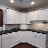 Bright corner kitchen view with shaker-style white cabinets, black counters, and modern tile backsplash