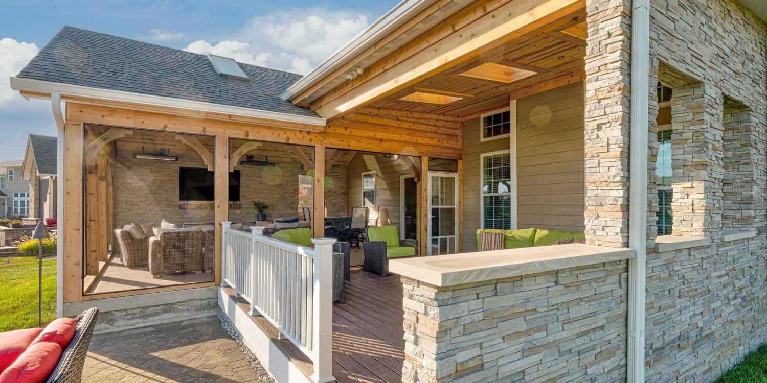 Covered backyard patio with wood ceiling, stone columns, seating area, and screened porch in Brownsburg, Indiana.