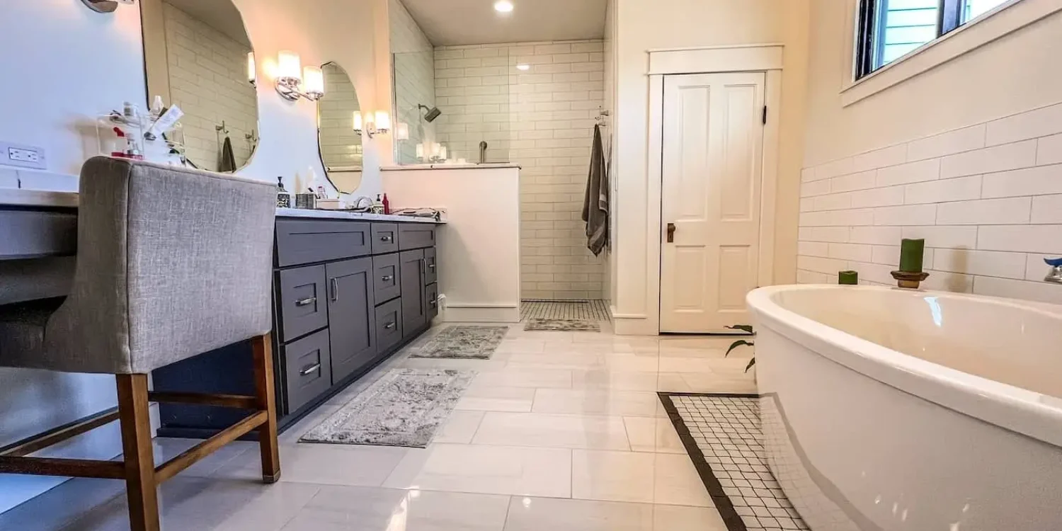 Bathroom with dual gray vanities, open wet room shower, and freestanding tub