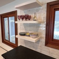 Floating white shelves displaying dishes and glassware against a textured white kitchen backsplash