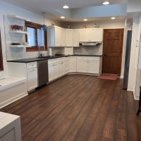 Wide view of a modern kitchen featuring white cabinets, black countertops, and rich wood flooring
