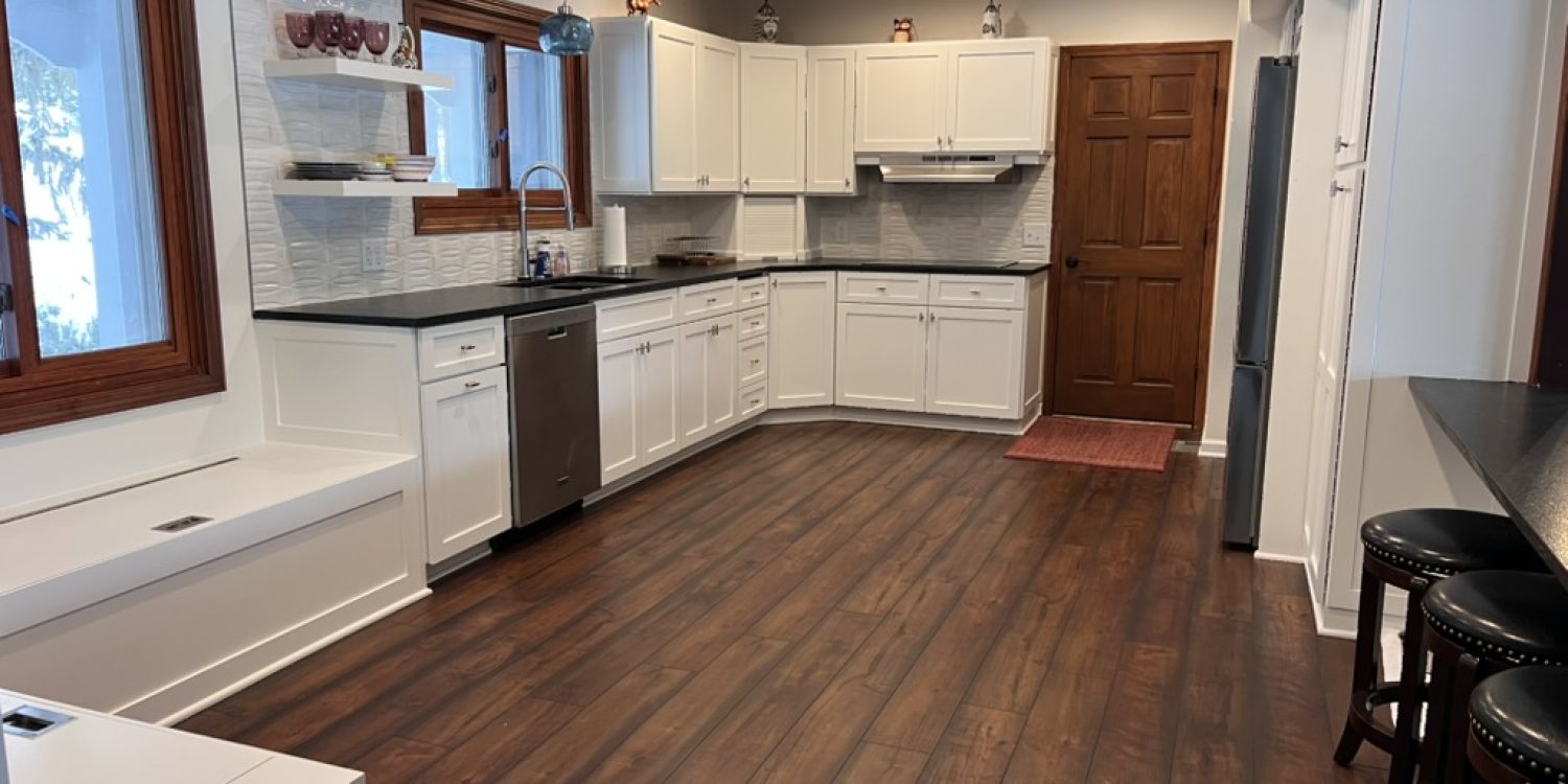 Wide view of a modern kitchen featuring white cabinets, black countertops, and rich wood flooring