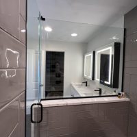 Glass shower enclosure with a view of double vanity and LED mirrors