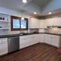 White kitchen wall cabinets and drawers with dark black countertops and tile backsplash