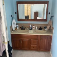 Straight-on view of a lake house bathroom before renovation, with dual-sink vanity, wood cabinets, large mirror, and light blue walls.