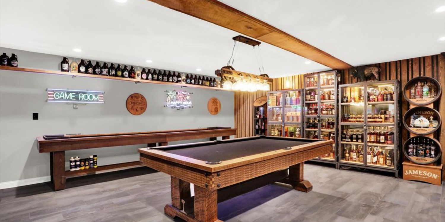 Stylish basement game room with pool table, shuffleboard, backlit bar and liquor display
