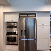 Front view of stainless fridge and wall ovens built into custom white cabinetry with wicker baskets above