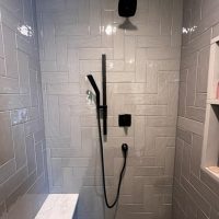 Close-up of gray tiled shower wall with matte black rain shower and hand wand