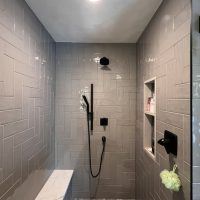 Close-up of gray tiled shower wall with matte black rain shower and hand wand