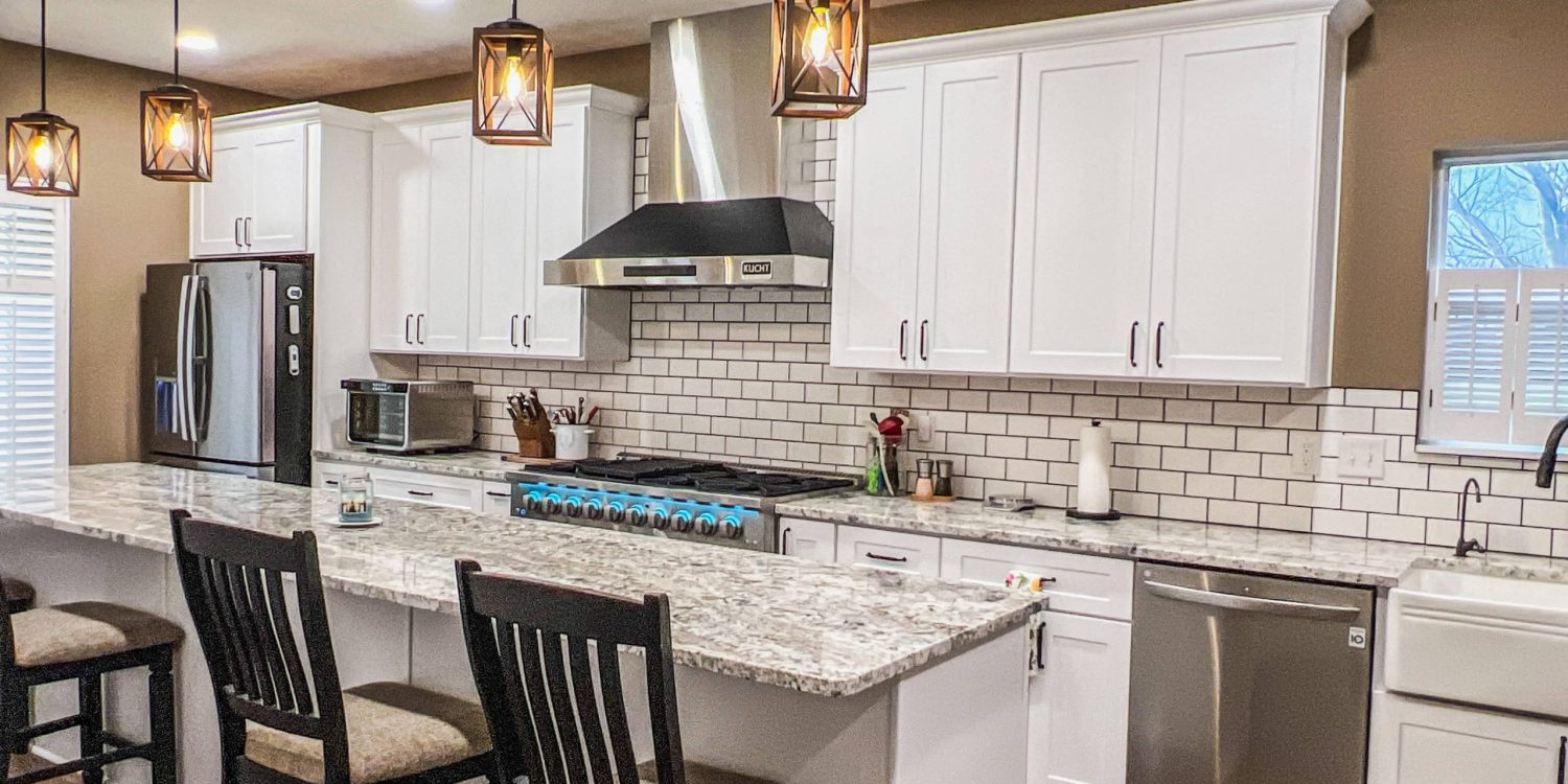 Modern kitchen interior with white cabinetry, stainless steel appliances, granite countertops, and pendant lighting over a central island with seating.