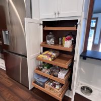 Pantry cabinet with multiple slide-out wooden shelves holding kitchen supplies and snacks