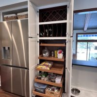 Open pantry cabinet with multiple wooden pull-out shelves storing snacks, jars, and containers