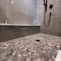Gray tiled shower with pebble floor and built-in marble bench