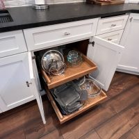 Pull-out kitchen cabinet drawers filled with glass and metal bakeware, organized for easy access