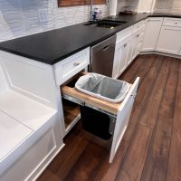 Under-counter pull-out trash and recycling bin in a white kitchen cabinet