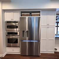 Stainless steel refrigerator and double wall ovens framed by white storage cabinets