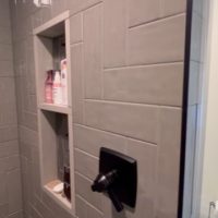 Close-up of shower niche with toiletries in a gray tile wall and black fixtures