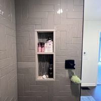 Walk-in shower with gray herringbone tiles, black fixtures, and built-in shelving niche